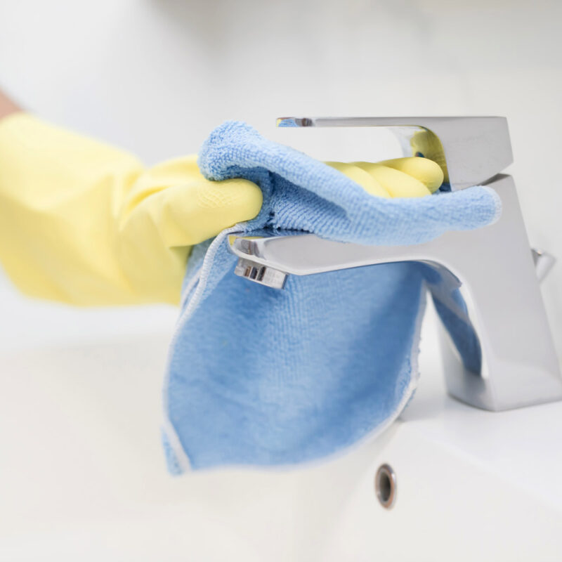 mano con guanto giallo che pulisce rubinetto del lavandino in bagno con un panno per la pulizia