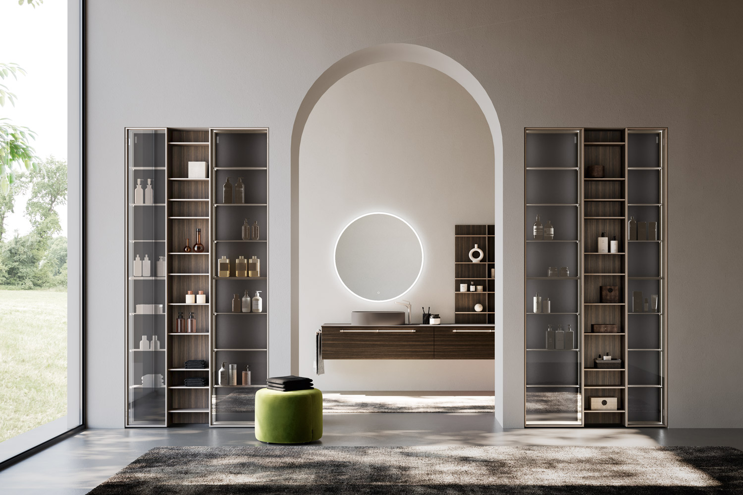 Bagno moderno di design con lavabo sospeso in legno scuro, specchio rotondo retroilluminato e scaffali con ante in vetro. Ambiente luminoso con arco centrale e sgabello verde su tappeto scuro.