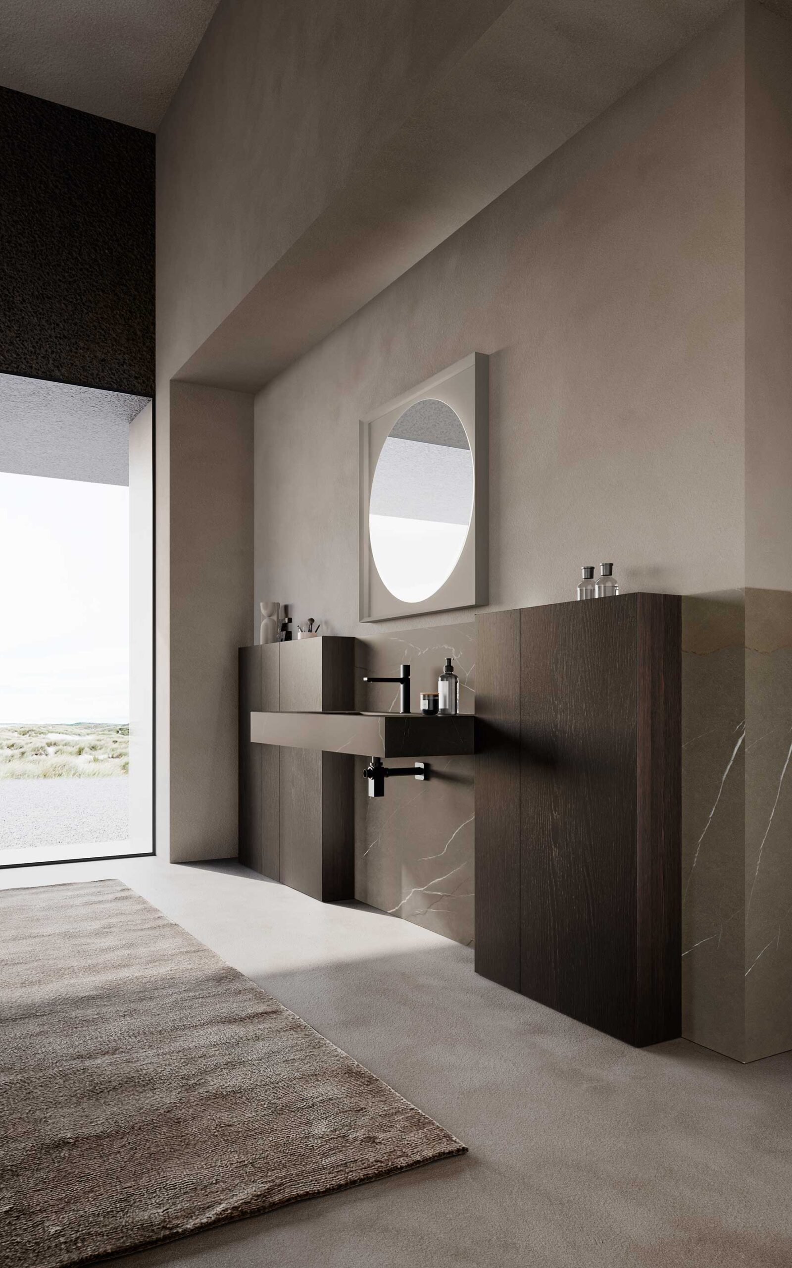 Side view of an elegant bathroom furniture composition with integrated washbasin top in Gres Pietra Piasentina Taupé, space-saving Wally storage units in Moka Oak veneer, round backlit mirror with square frame.