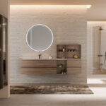 Arredo bagno moderno Azzurra Lime 1.0 con mobile sospeso in melaminico Dekorativo 3D effetto legno, lavabo integrato, vani a giorno, specchio rotondo retroilluminato e doccia walk-in in un ambiente dal design minimalista.